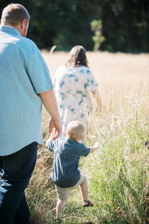 Family walks together through a sunlit field of tall grass at sunset creating a peaceful outdoor silhouette.