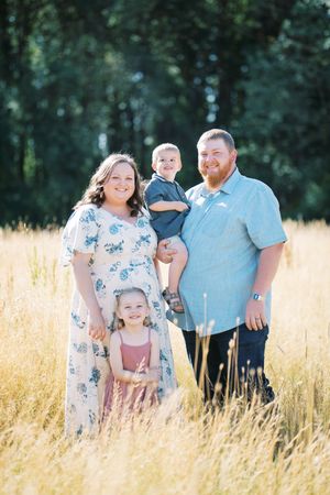 Family portrait in a golden wheat field surrounded by green trees on a sunny summer day.