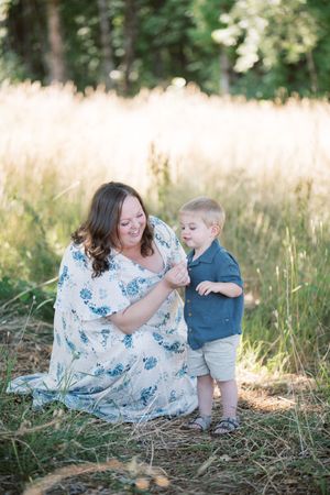 A parent and child share tender outdoor moments together in a sunlit meadow with tall grass.