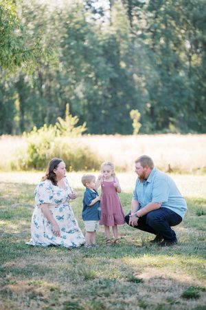 A family enjoys a warm summer evening together in a sunlit meadow surrounded by trees.