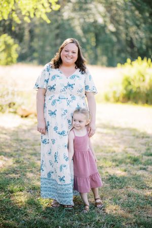 Parent and child stand together outdoors in a sunny field wearing floral maxi dress and pink ruffled dress.