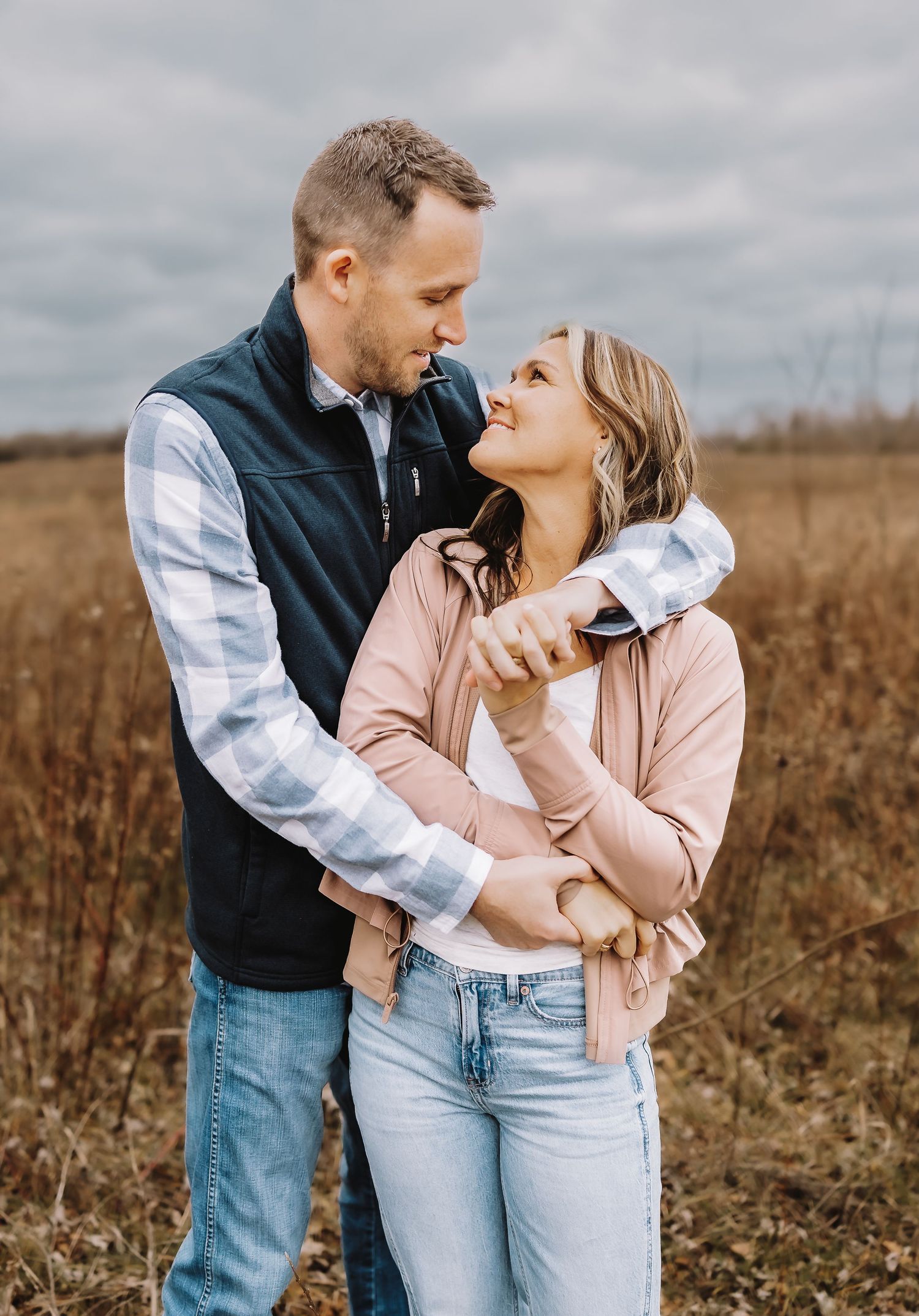 A couple shares romantic moments in a fall field wearing jeans and casual attire.