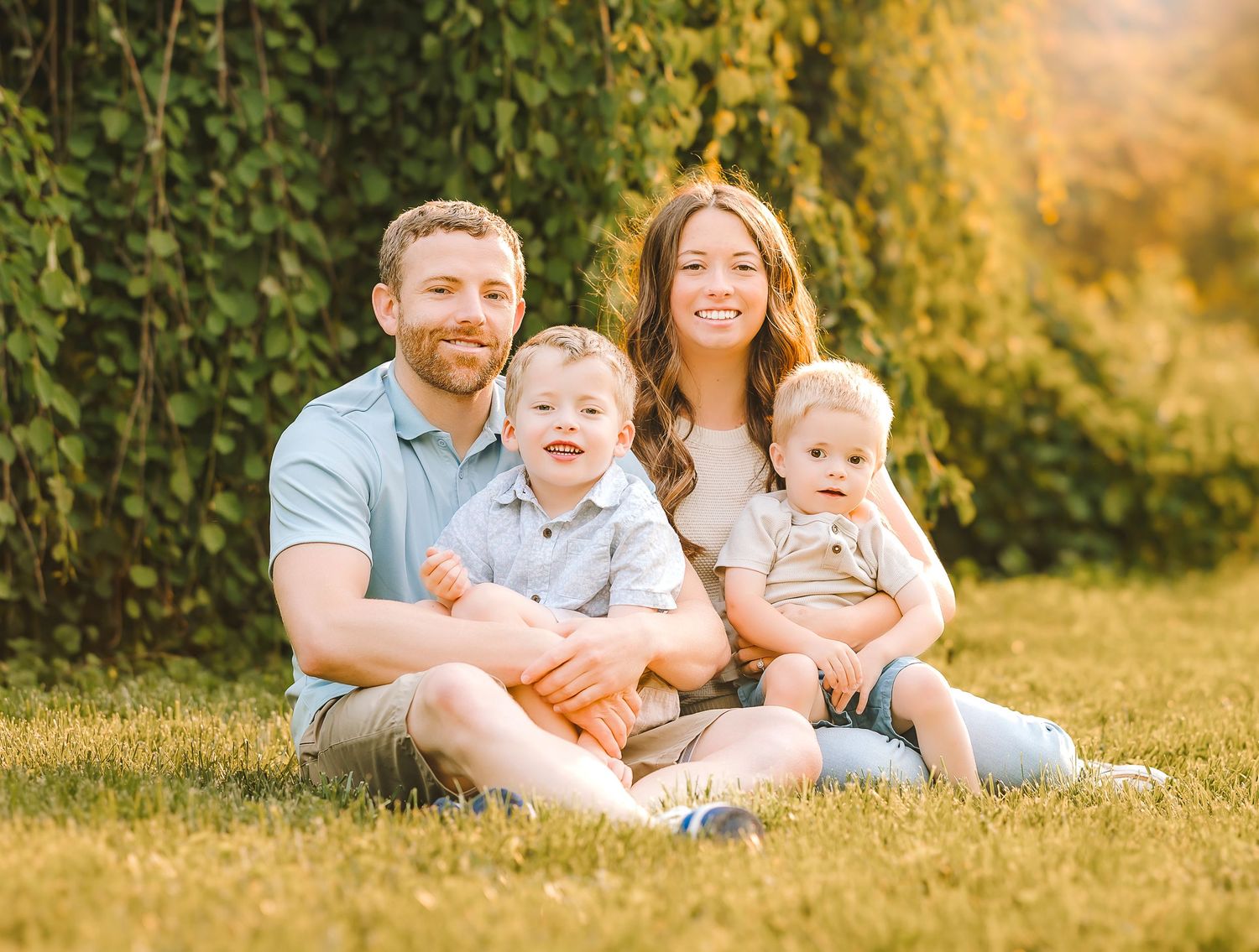 Happy family relaxes together during an outdoor sunset photo session in a grassy meadow.