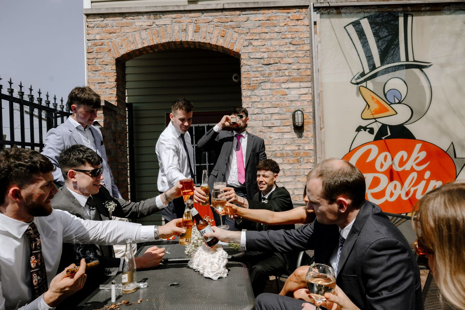 A celebratory summer wedding scene with guests toasting and clinking champagne glasses during an outdoor reception.