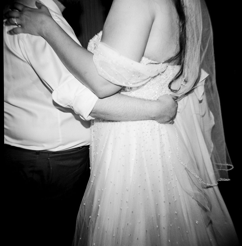 Black and white 120mm holga film photo detail of couple holding each other while dancing at their wedding reception in Portland, Maine.