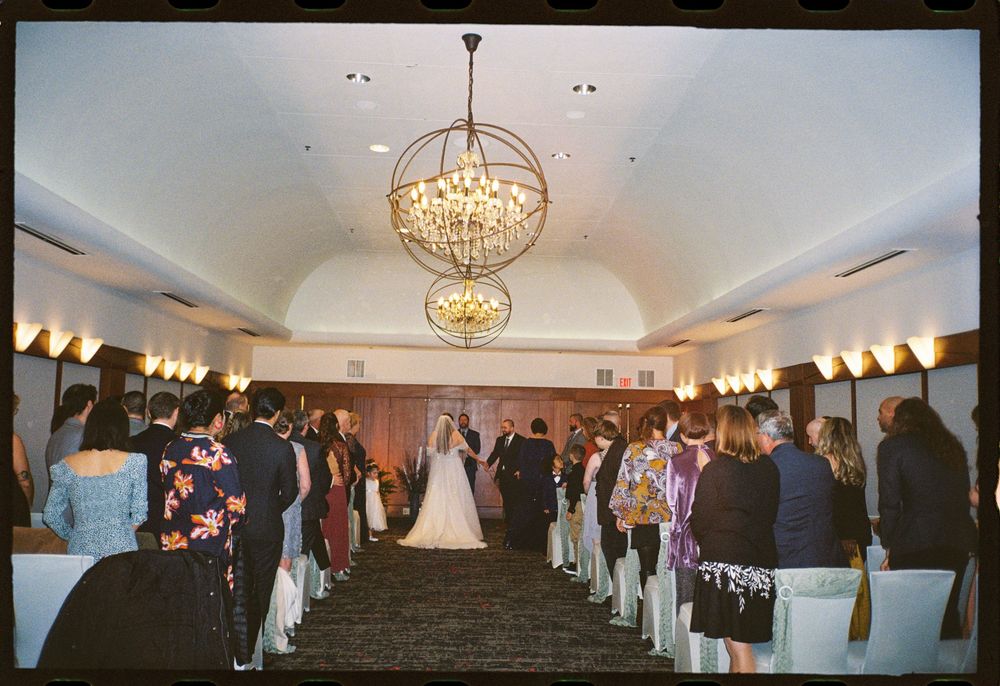 The guests stand as the bridal party walks down the aisle at winter wedding ceremony held at The Regency Hotel in downtown, Portland Maine.