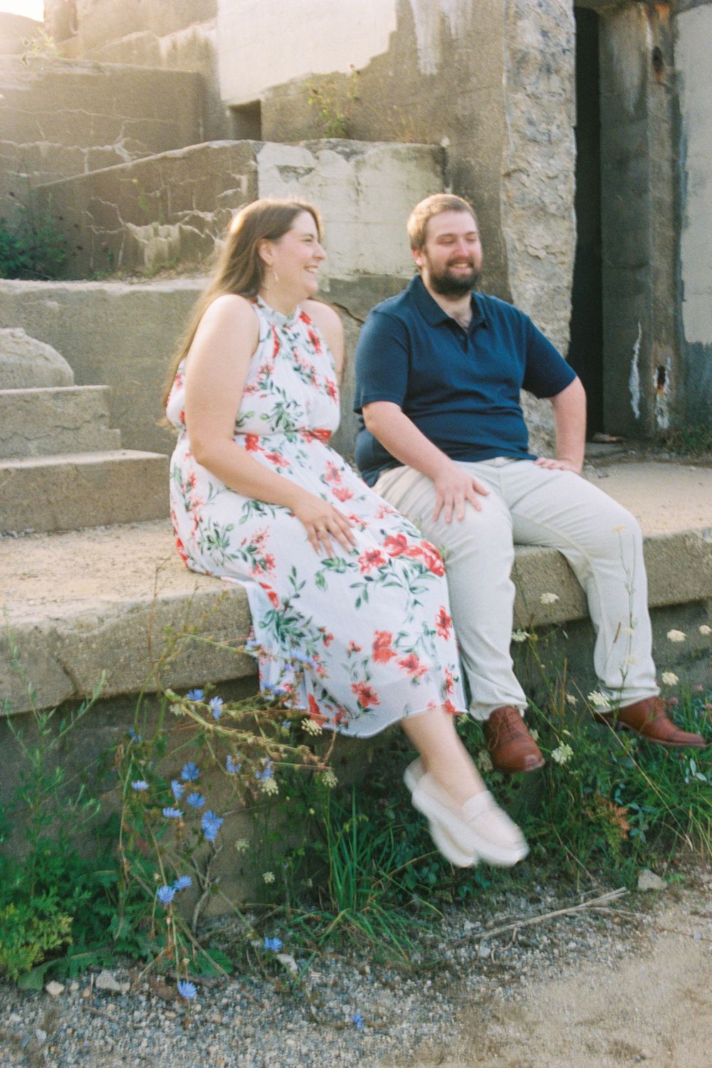Engaged couple poses and laughs together in the early morning sunshine at an old fort in a park in Cape Elizabeth, Maine.