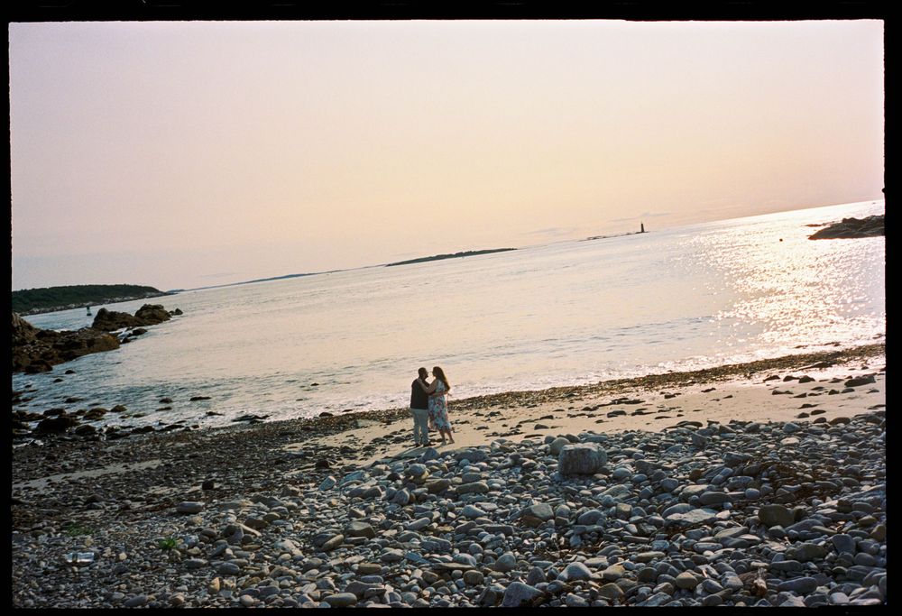 Landscape photograph of couple holding each other on the beach in the early morning light in Fort Williams park in Cape Elizabeth, Maine.