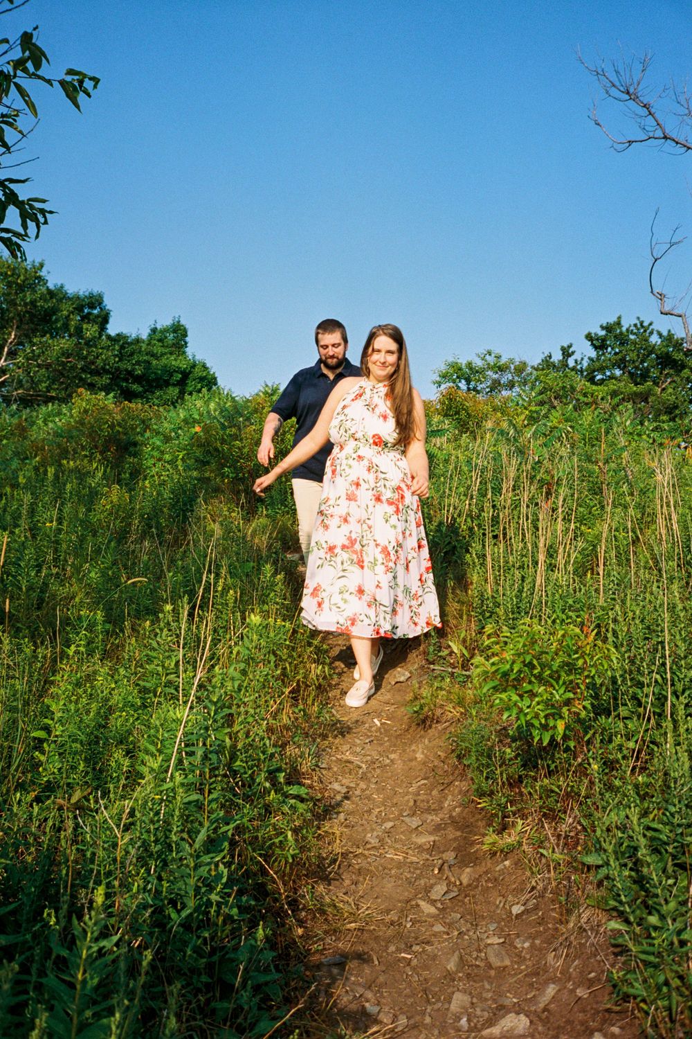 Couple walking through the grass laughing and smiling for their engagement photos in a park in southern Maine on analog film.