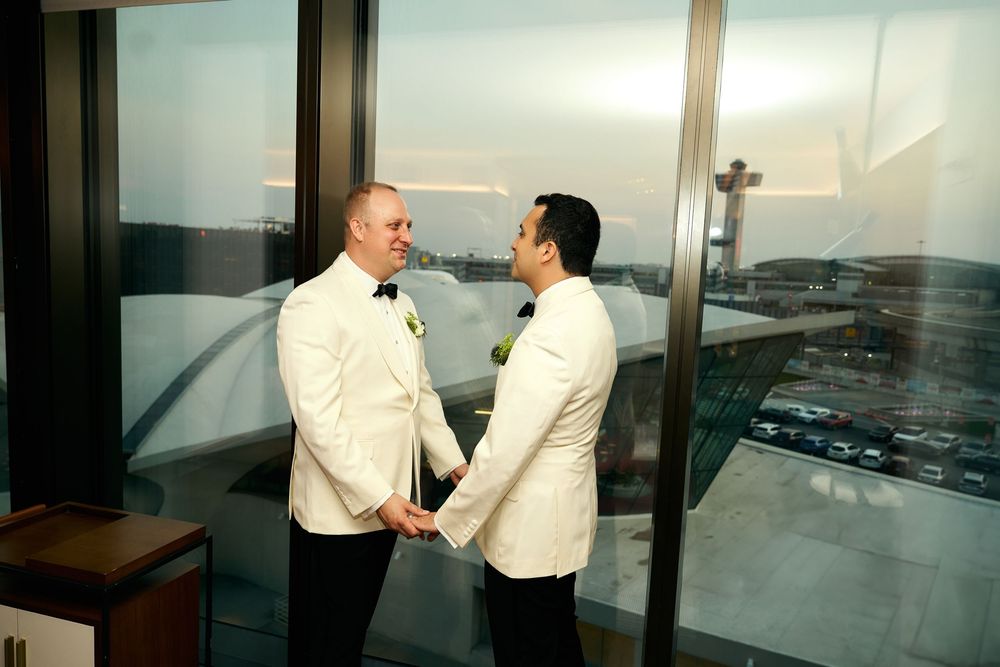 Series of panoramic windows overlooking an urban cityscape with people in formal attire. gay couple wedding  TWA hotel