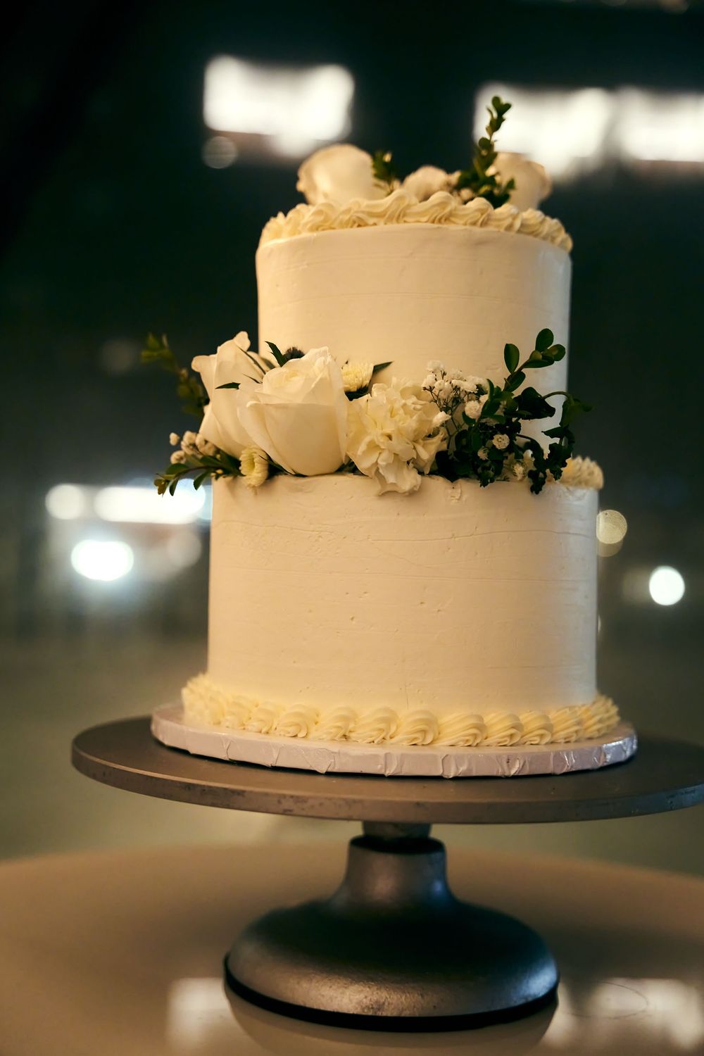 Elegant white wedding cake decorated with delicate flowers on a dark pedestal stand. wedding  TWA hotel