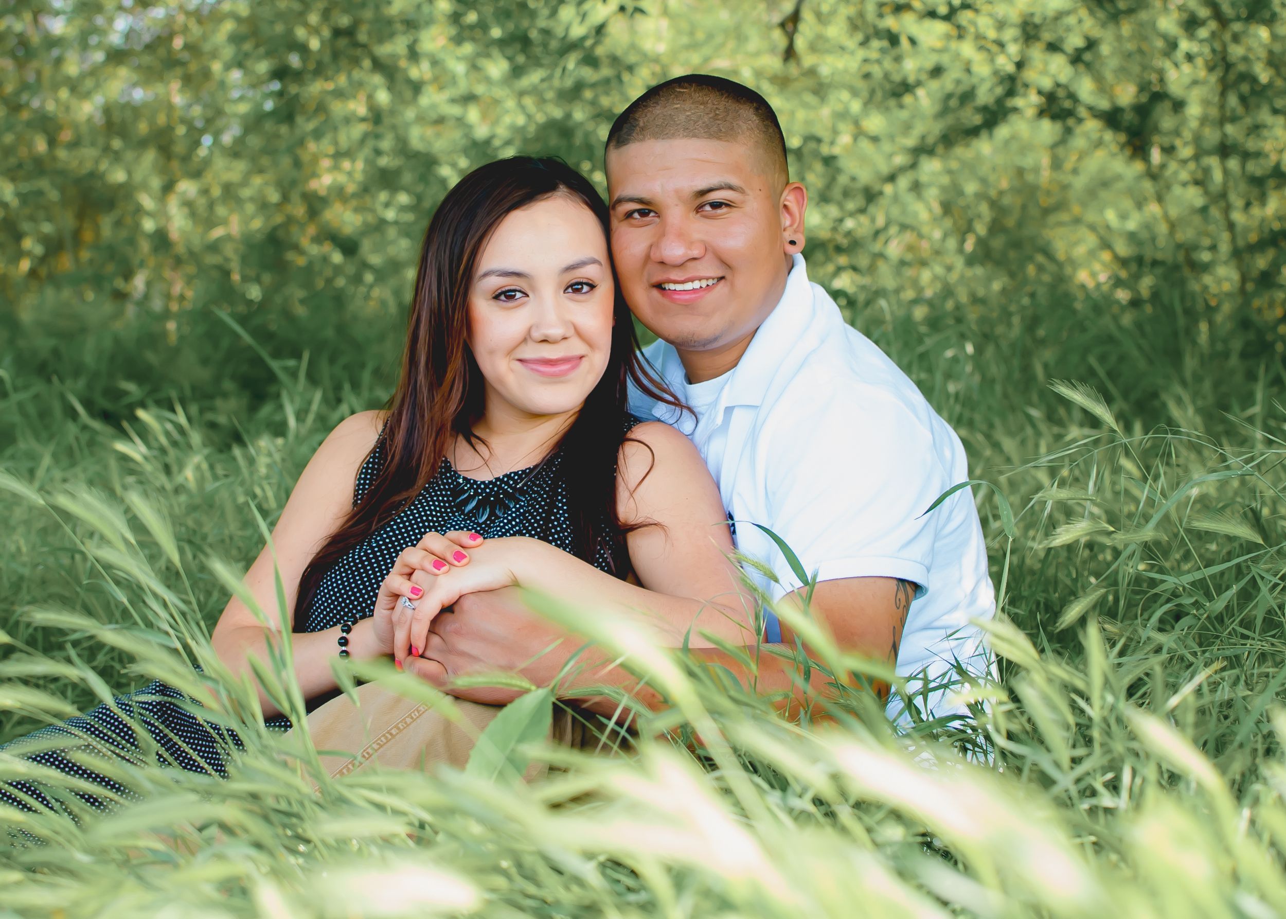 A couple poses romantically together in tall green grass and natural lighting during an outdoor photo session.