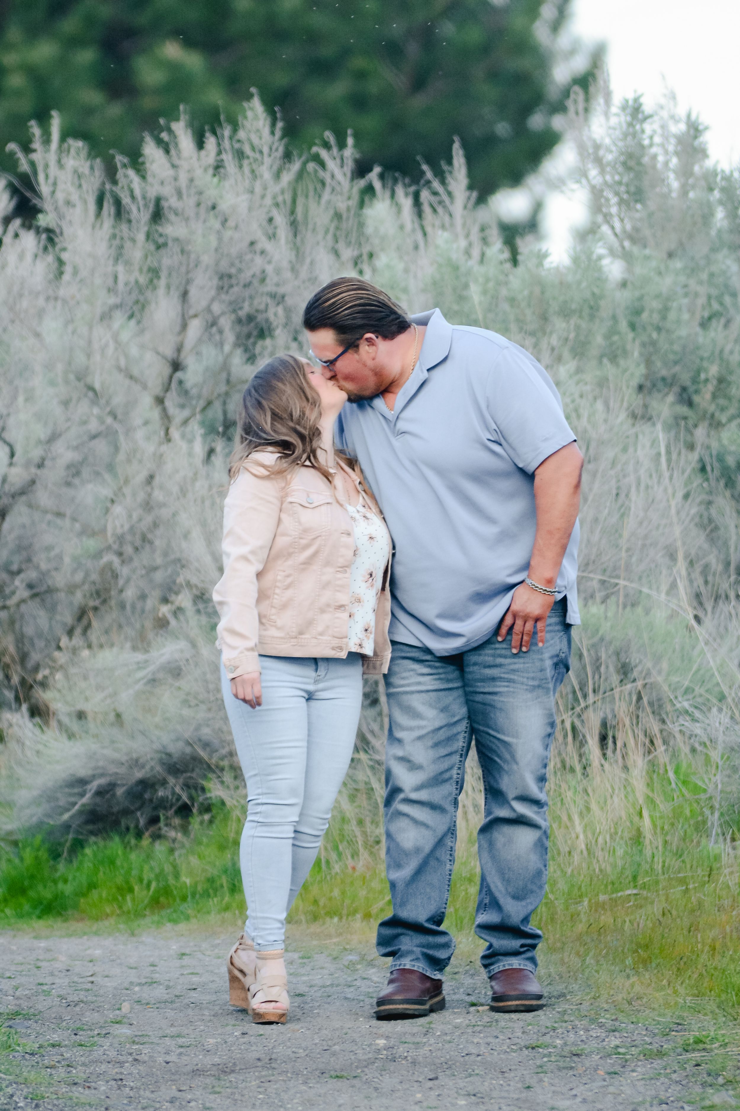 A couple shares a romantic countryside moment together among tall grass and wildflowers during a photoshoot.