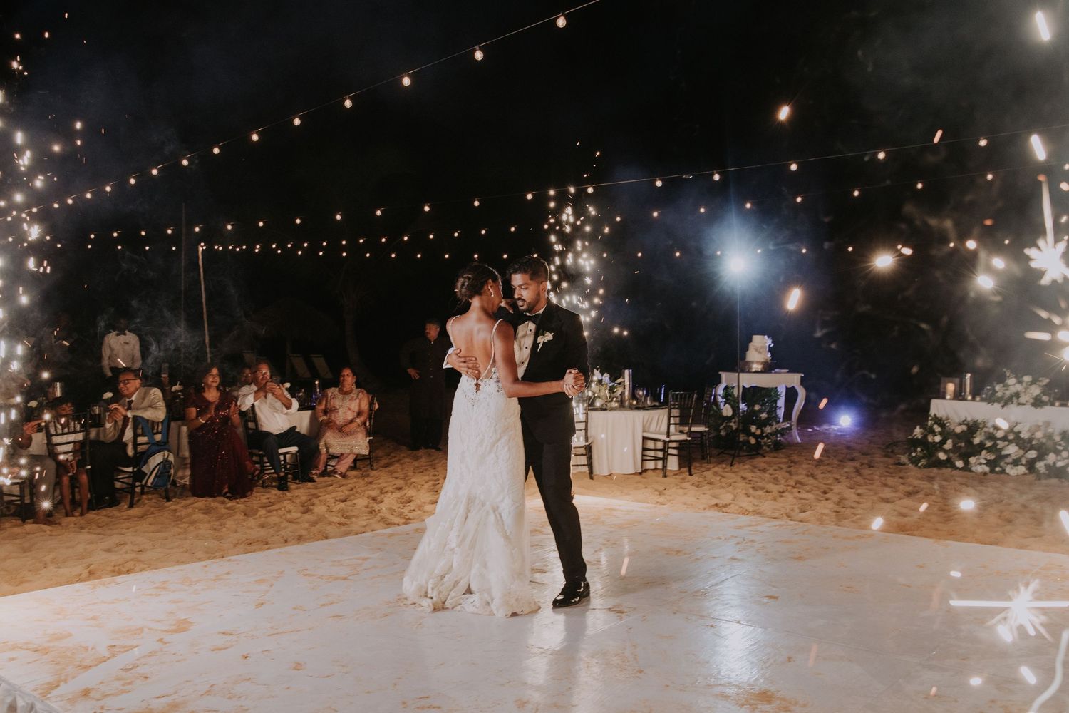 String lights illuminate an outdoor wedding dance floor during evening celebration.