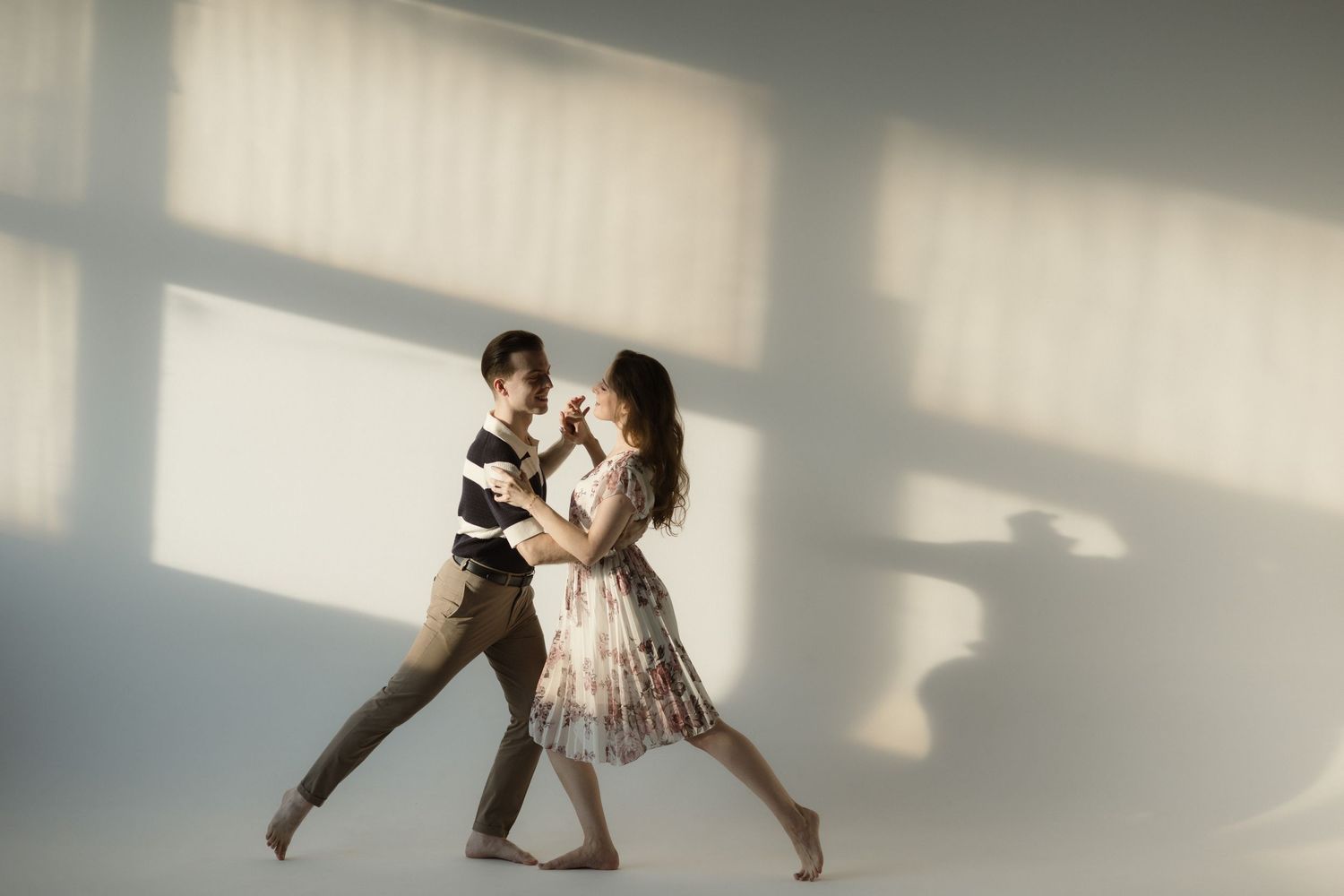 Contemporary dancers performing expressive movements in a light-filled studio with dramatic shadows and angles.
