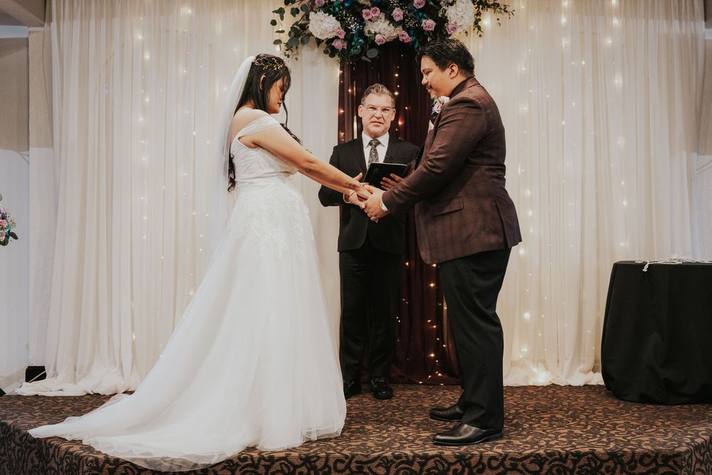 A joyful wedding ceremony moment captured in front of white curtains with twinkling lights.