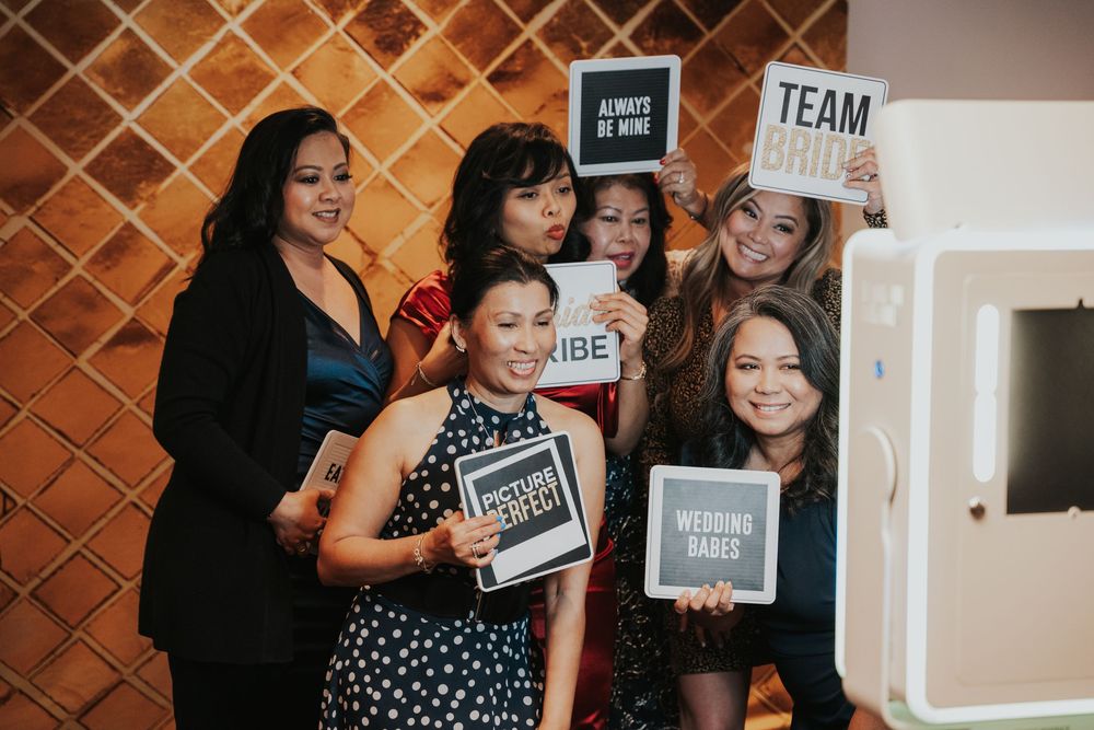 A group poses together holding small chalkboard signs at a photo booth with a diamond pattern wall background.