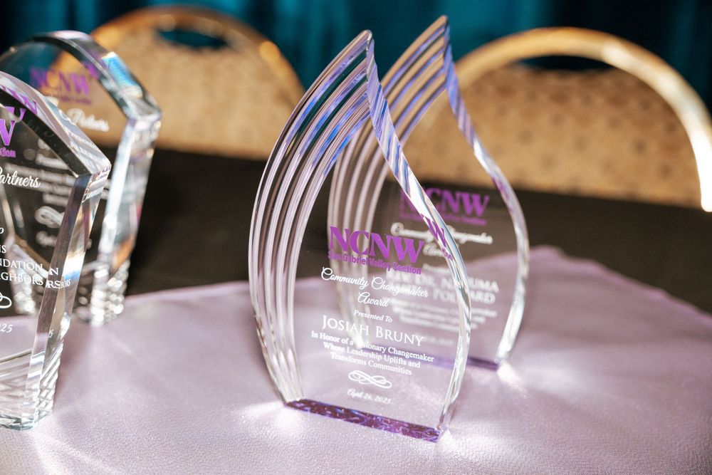 Clear acrylic flame-shaped award trophies with purple text displayed on a light purple tablecloth.