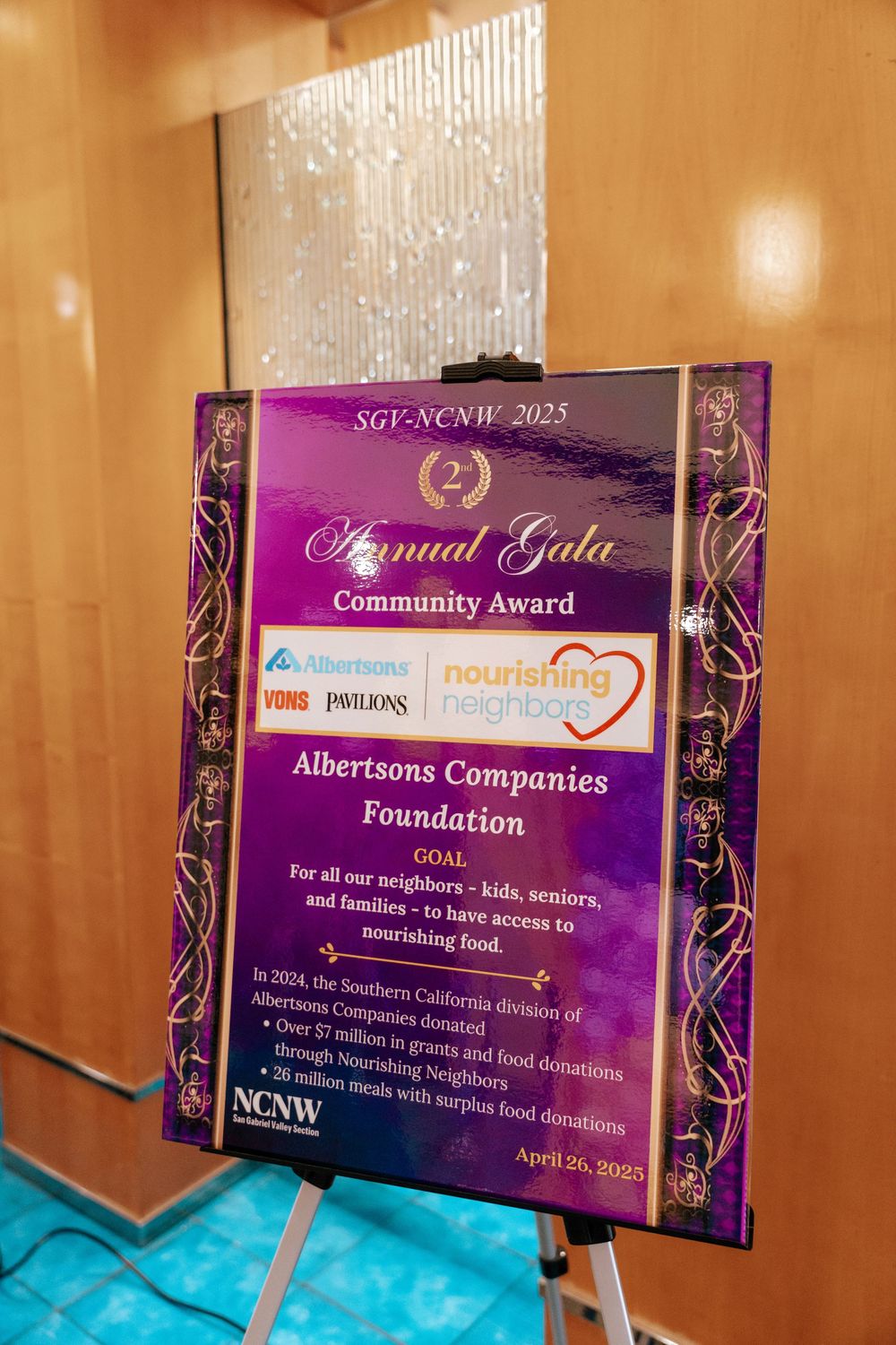 A purple and gold community award plaque for Albertsons Companies Foundation displayed on an easel at an annual gala event.