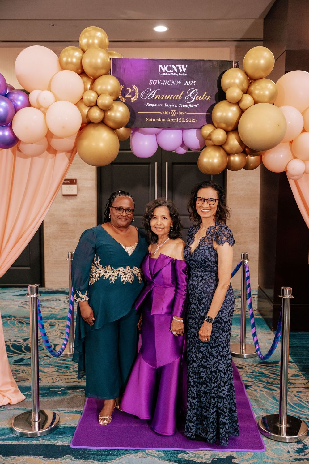Elegant gala event setup with balloon arch in gold, pink and purple colors against a purple banner backdrop on purple carpet.