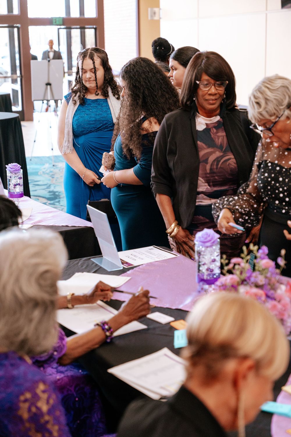 People gather around tables at an event signing documents and engaging in conversation.