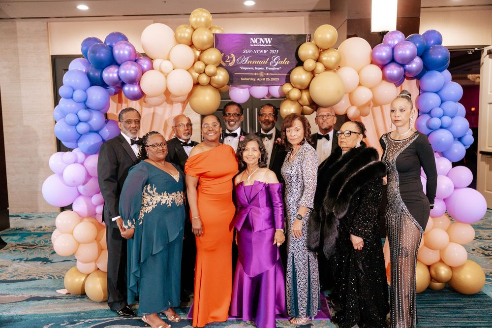 Group photo at formal event with elegant balloon arch featuring purple, gold and peach colors.