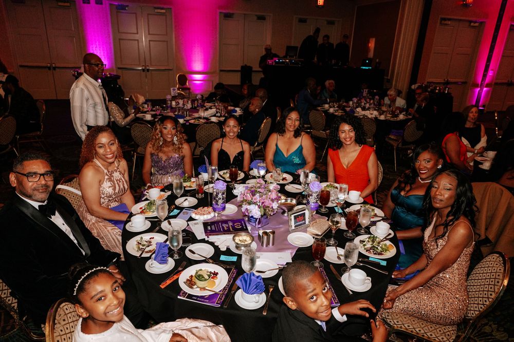 Guests seated at round tables during an elegant evening reception with pink and purple ambient lighting.