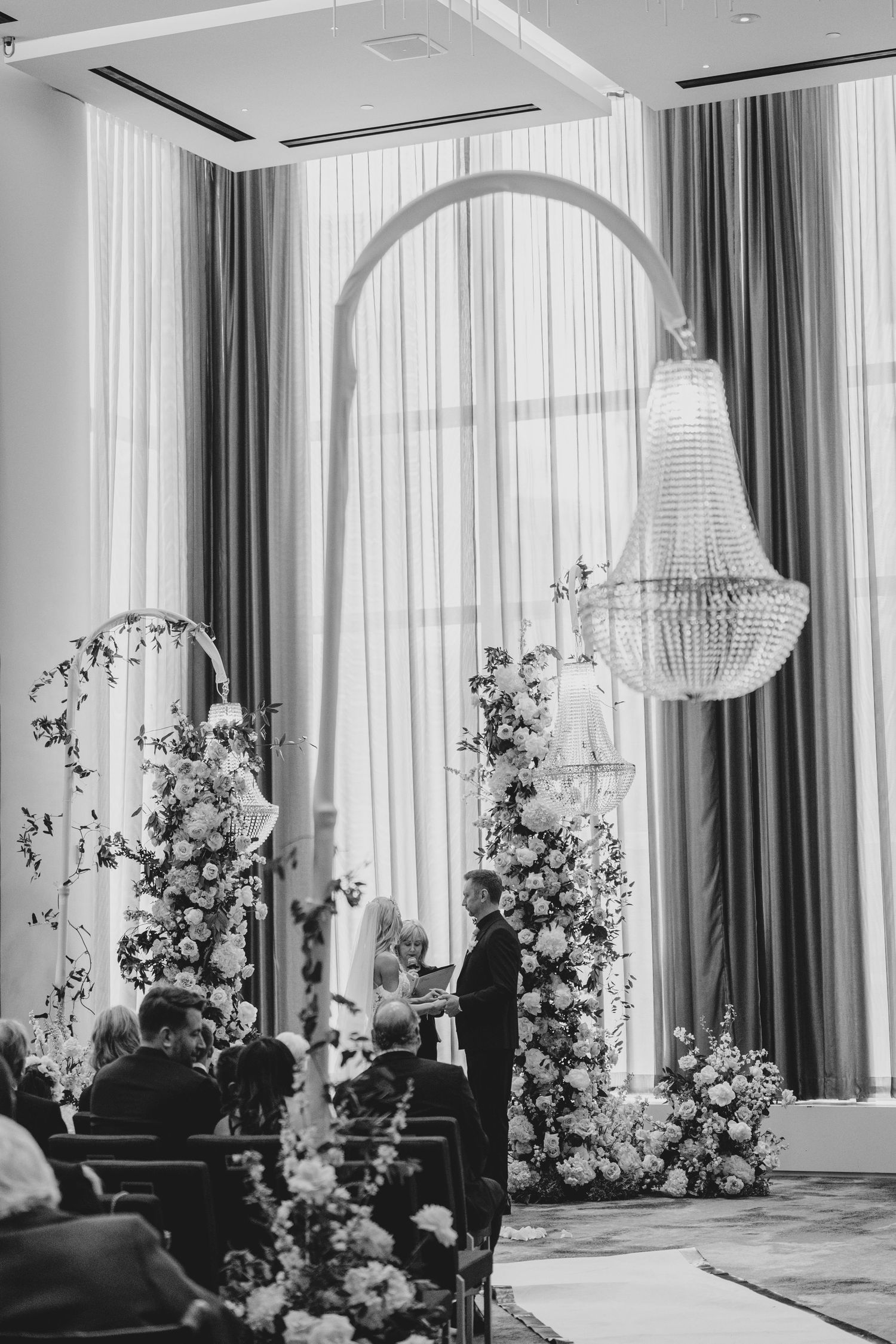 Elegant indoor wedding ceremony space with white floral arrangements and crystal chandeliers creating a romantic atmosphere.