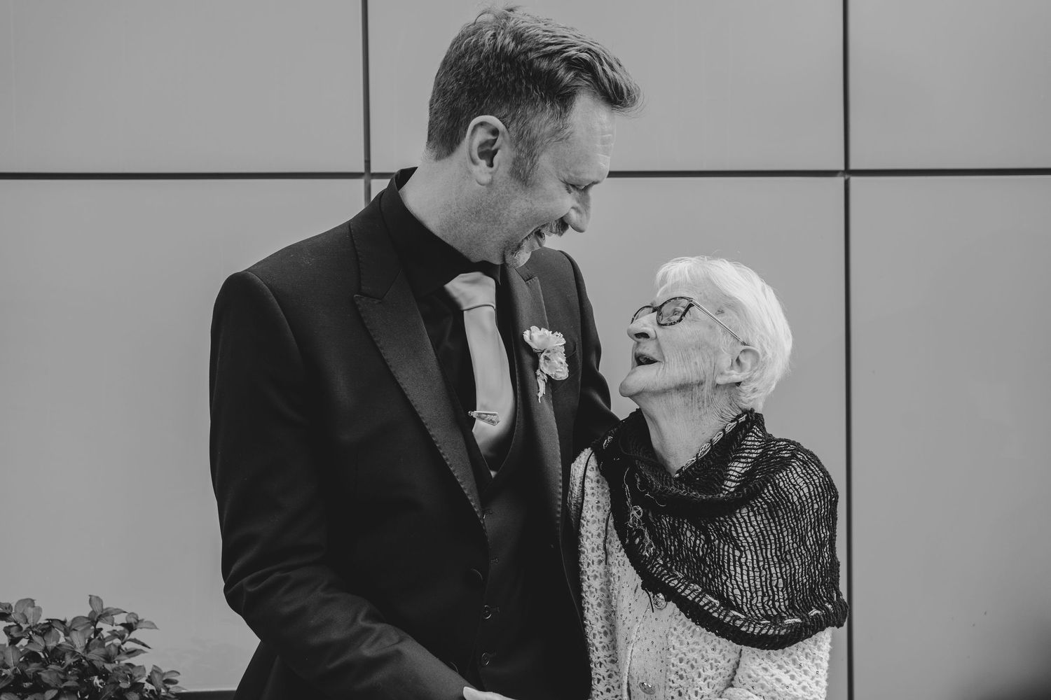 A black and white candid moment of a sweet exchange between loved ones during a wedding celebration.