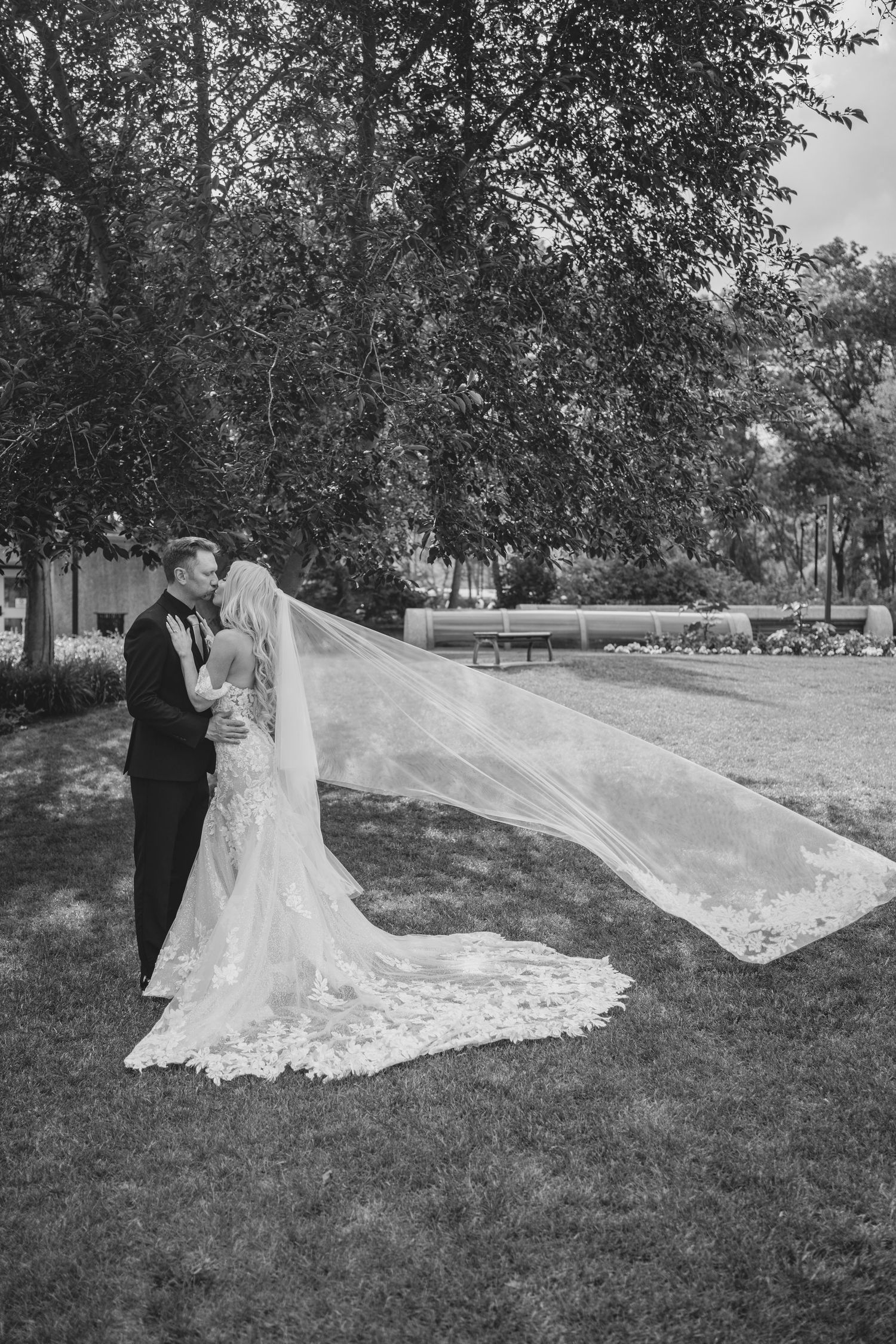 A romantic wedding scene outdoors with a flowing lace gown and long veil catching the breeze.