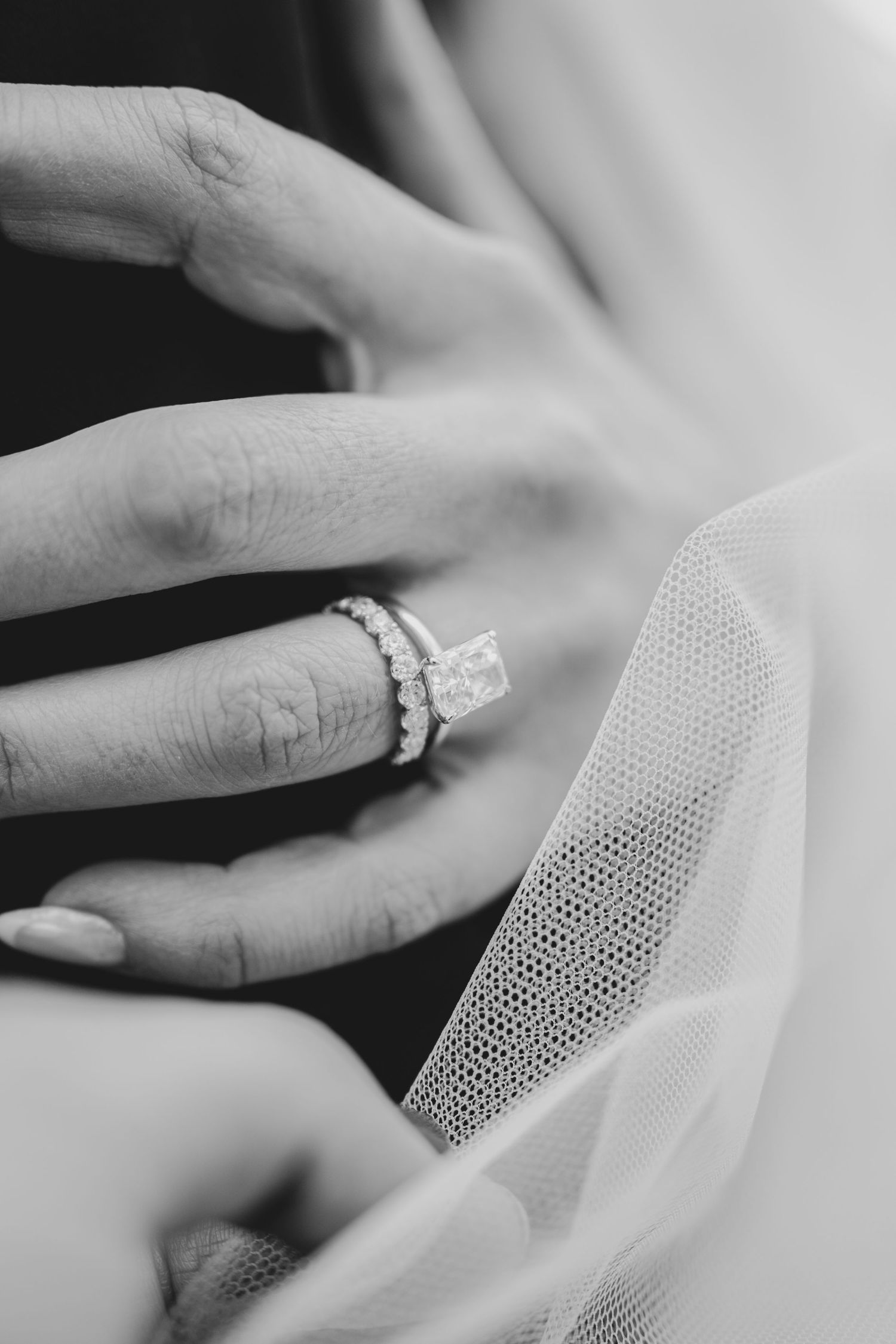 Close-up of a bride's hand showing her diamond engagement ring and wedding band against delicate tulle veil.