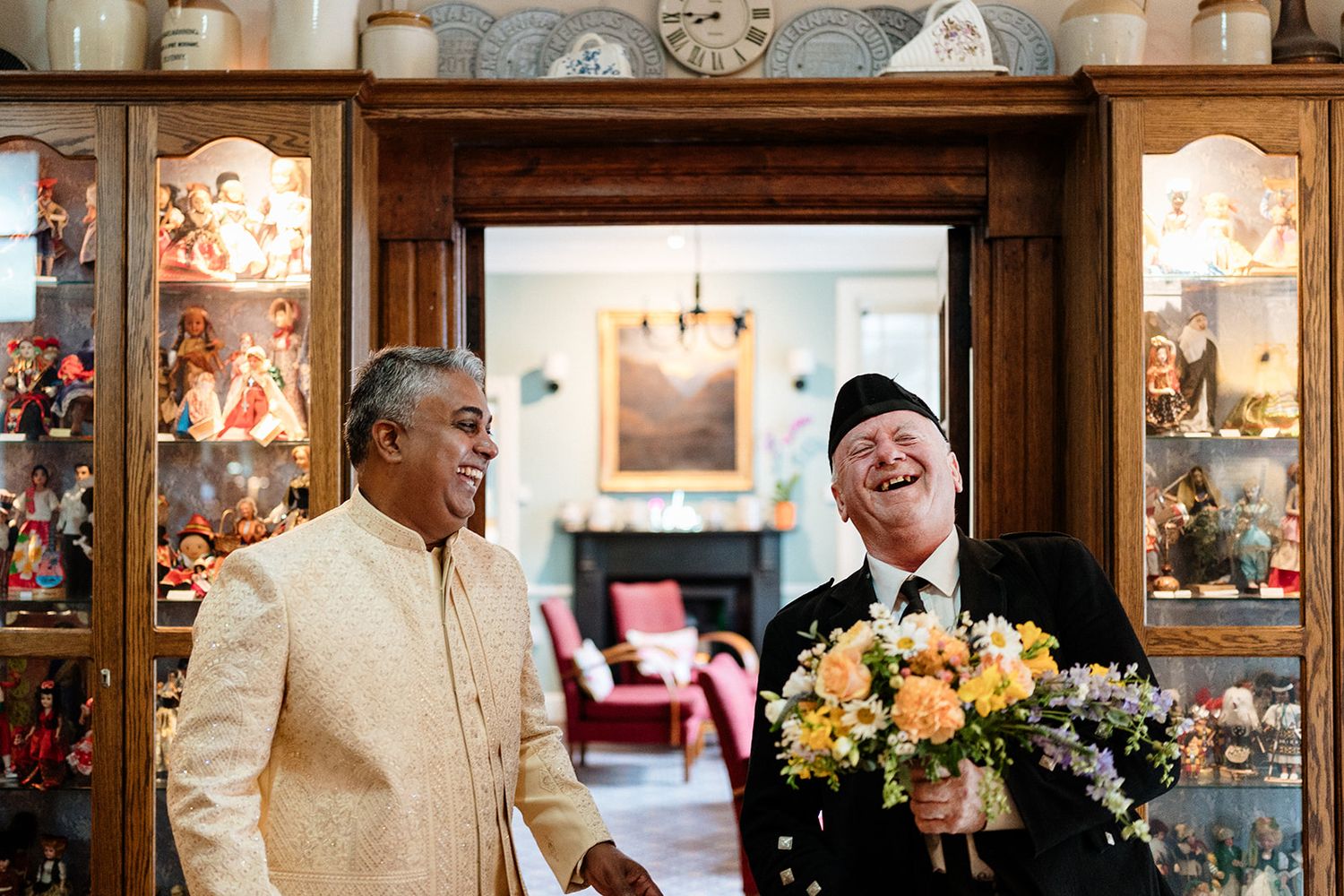 Two guests share a laugh together beside cabinets of glassware while one holds a yellow floral arrangement.