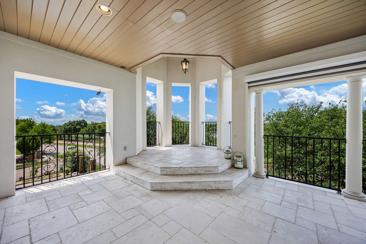 Elegant master bathroom with marble floor featuring a raised corner tub surrounded by panoramic windows overlooking green scenery.