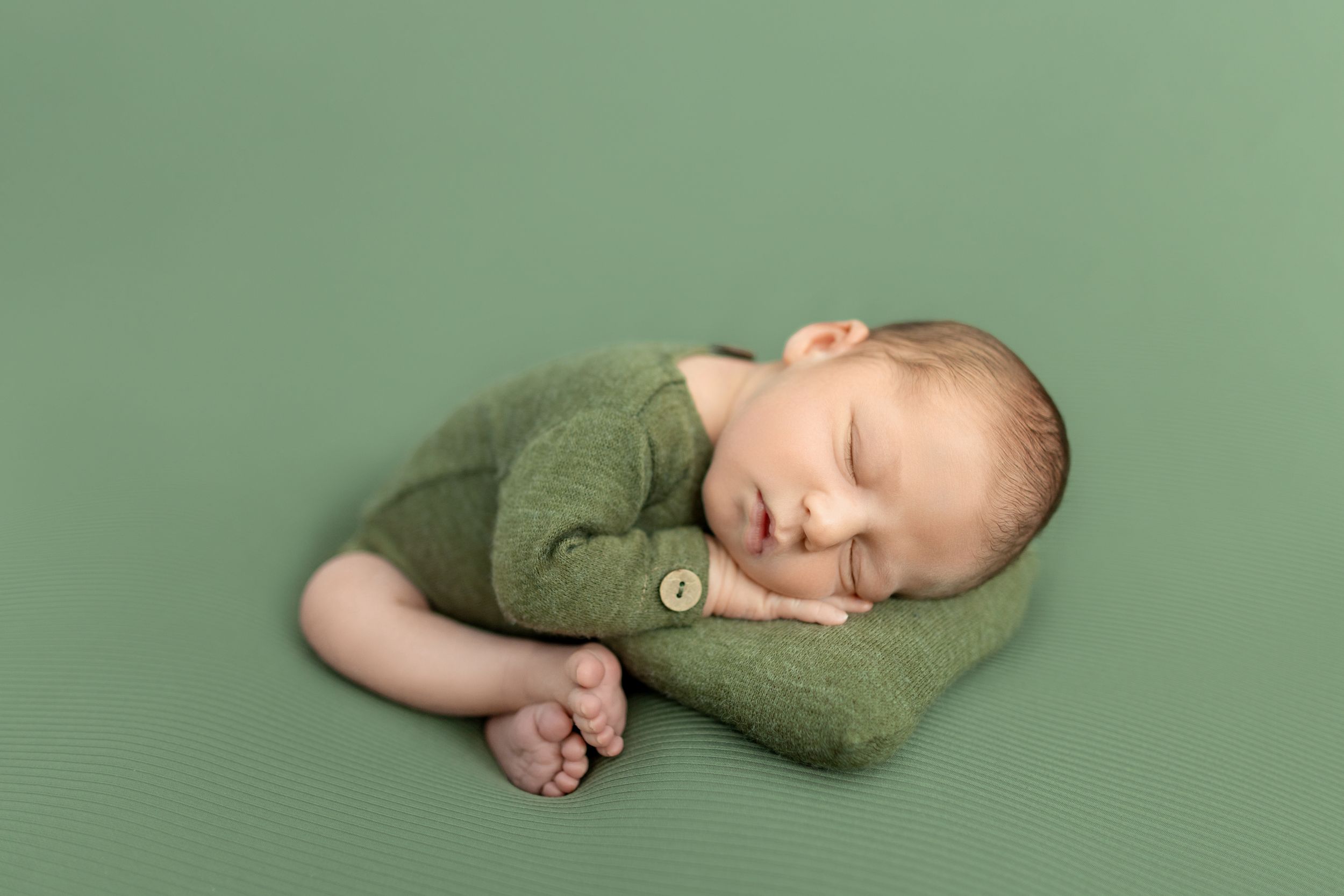 Newborn in olive green wrap posed peacefully on green background. Photos by Tampa Photographer DigitalMyst Photography