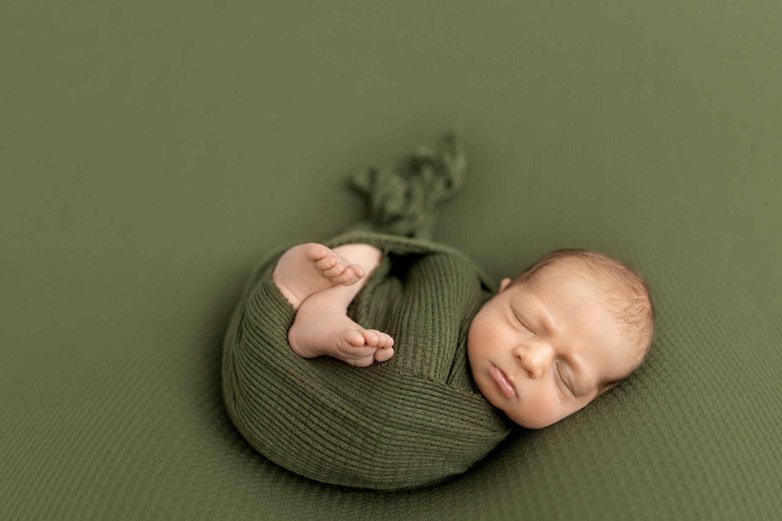 Baby wearing olive green bonnet sleeping on textured green backdrop. Photos by Tampa Photographer DigitalMyst Photography