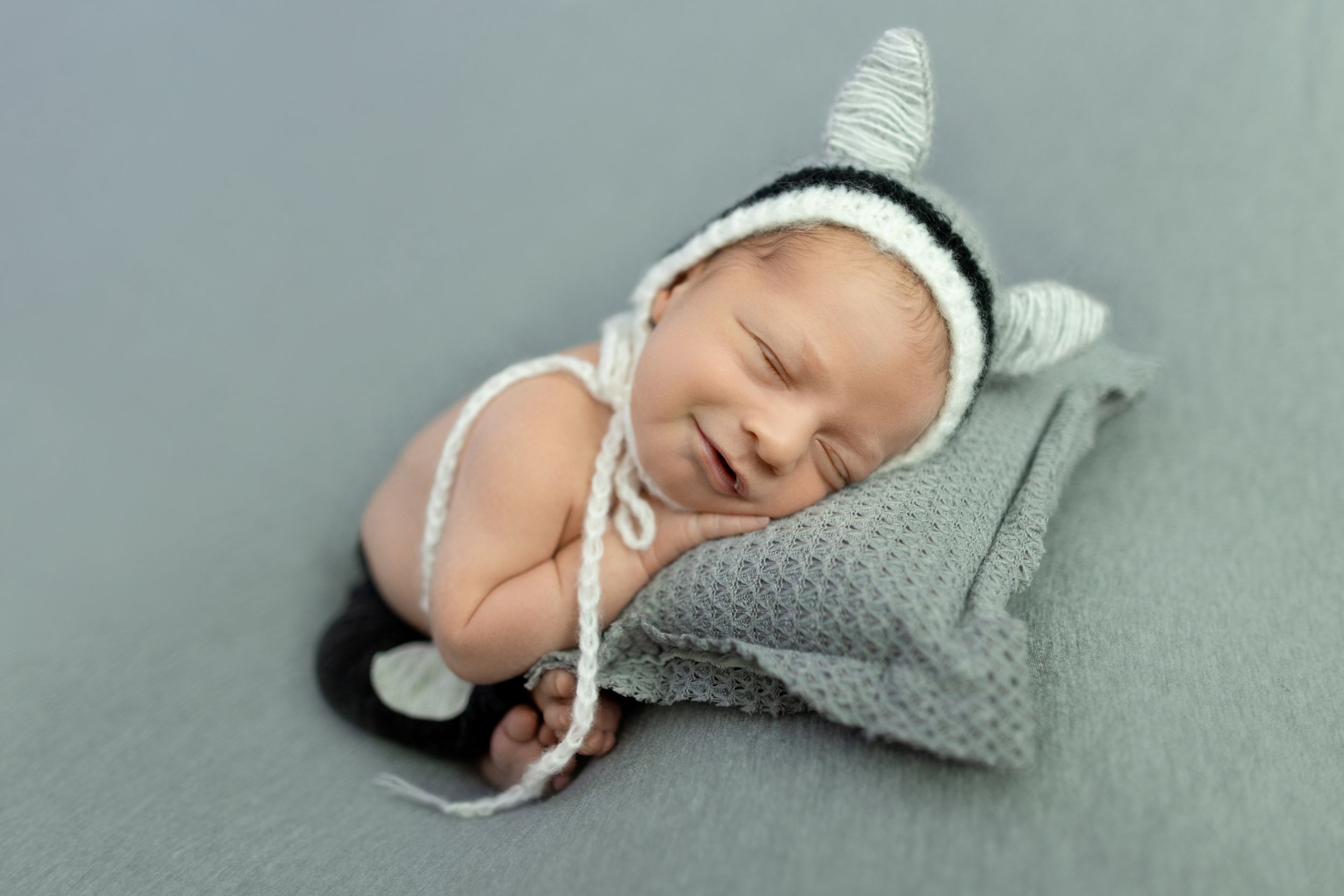 Newborn in gray knit outfit sleeping on light gray backdrop. Photos by Tampa Photographer DigitalMyst Photography