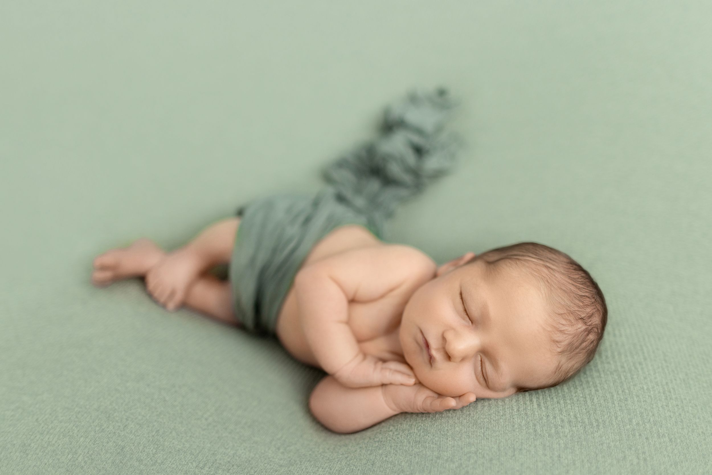 Sleeping newborn wearing sage green outfit laying on matching textured backdrop. Photos by Tampa Photographer DigitalMyst Photography