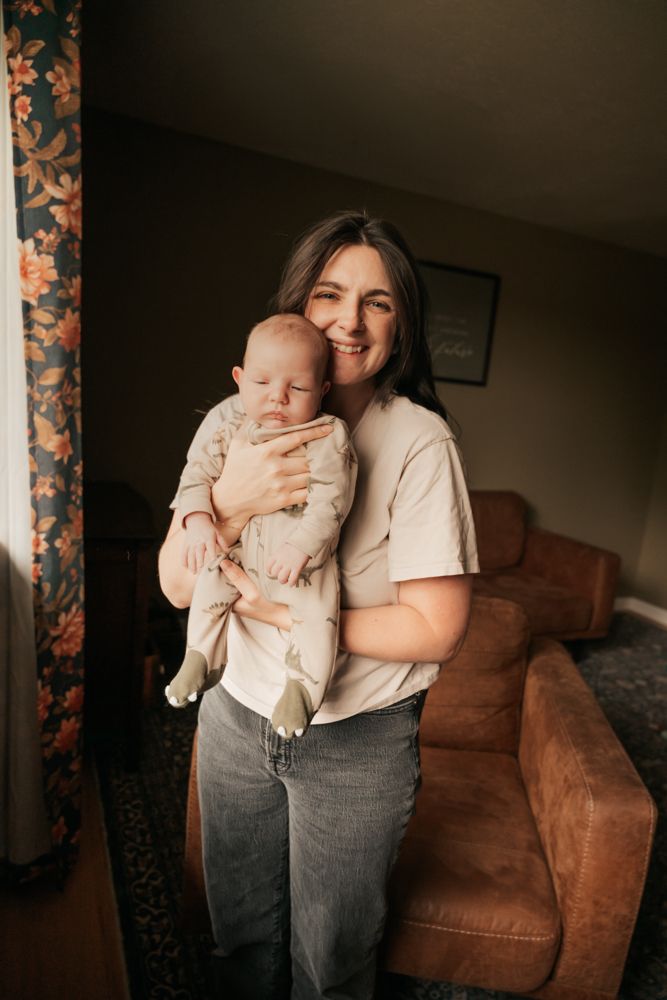 A parent and baby share a joyful moment together in a cozy living room with warm lighting and a brown sofa.
