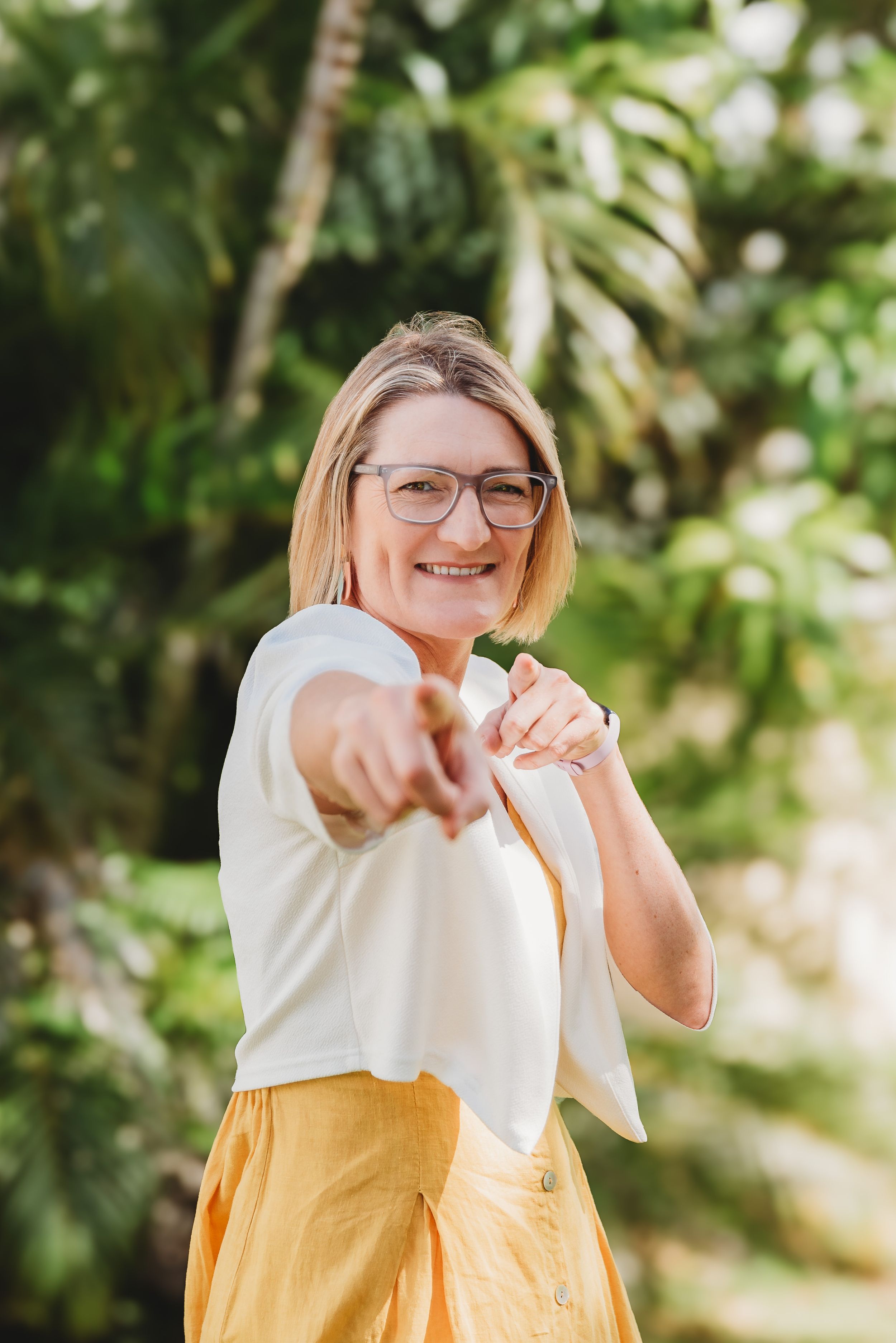 Person in yellow dress and glasses playfully motions and points outdoors in a series of dynamic poses.