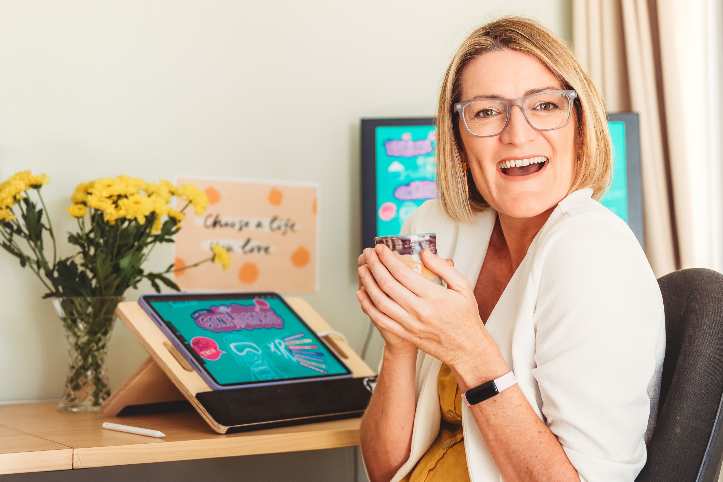 Professional sitting at desk with mug, tablet device, and yellow flowers in vase showing workspace setup.