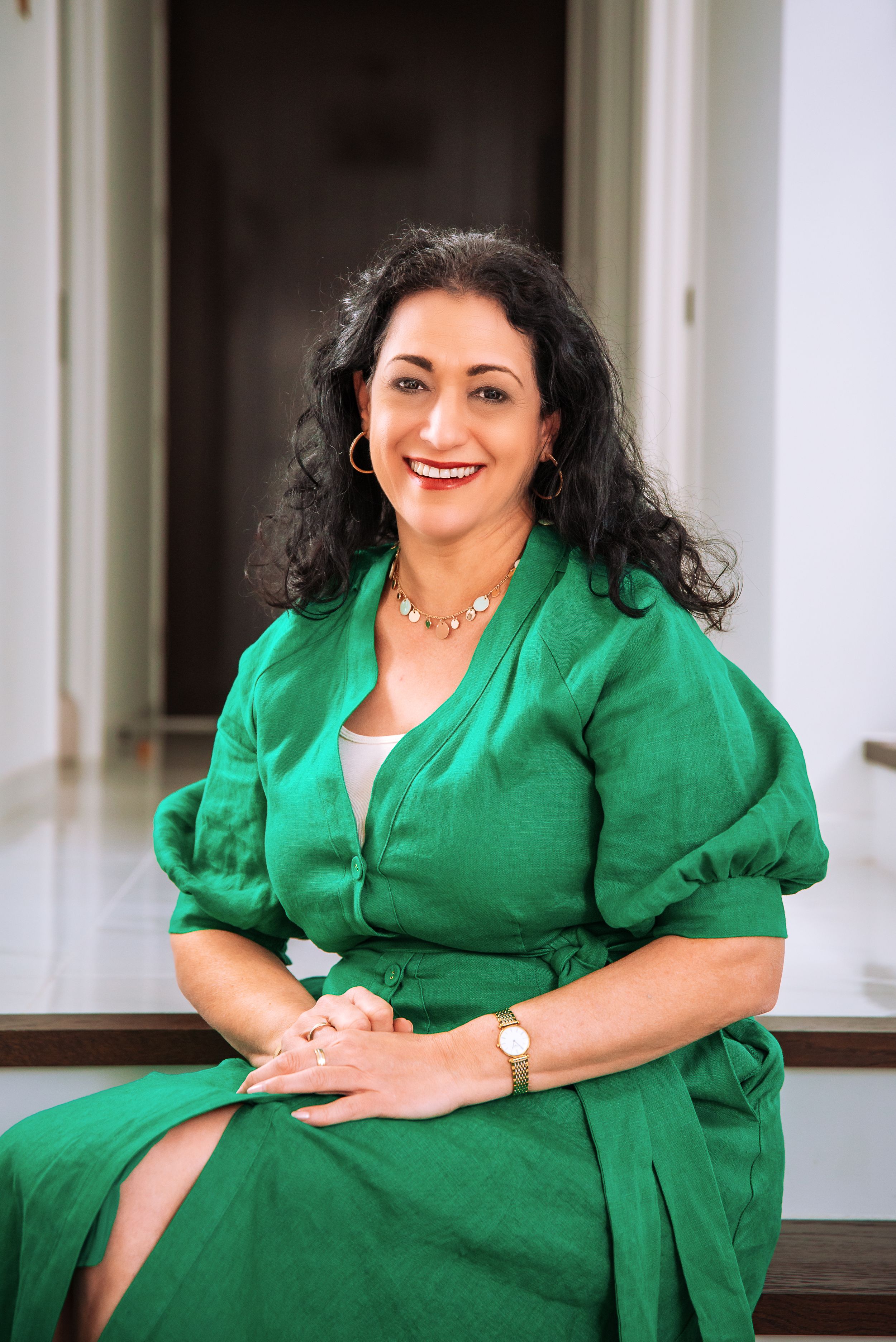 A woman in a vibrant green dress with puff sleeves sits smiling on outdoor steps.