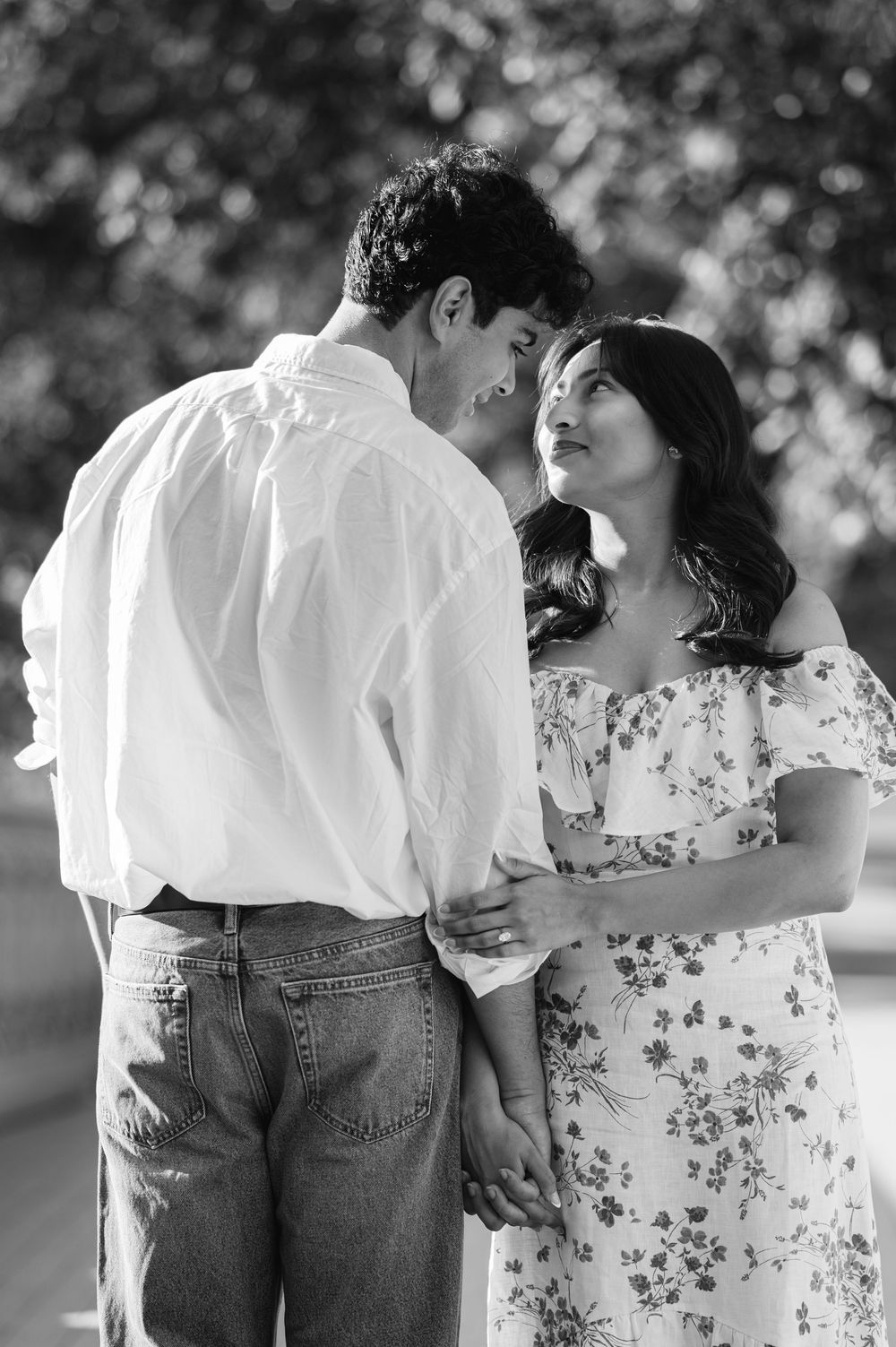 A romantic black and white photo of a couple in casual attire gazing at each other outdoors with soft bokeh lighting in Central Park.