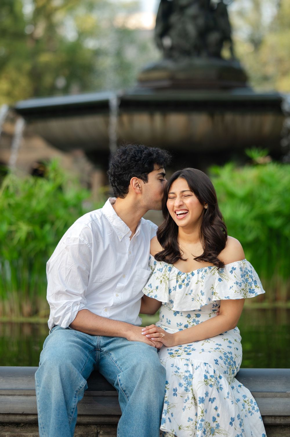An engaged couple shares a joyful moment while sitting together in front of Bethesda Fountain in Central Park during a proposal session