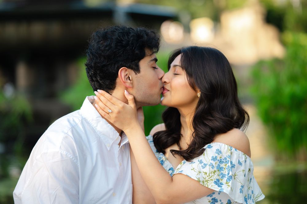 A couple shares a romantic kiss while showing off a new engagement ring during a proposal at Bethesda Fountain.