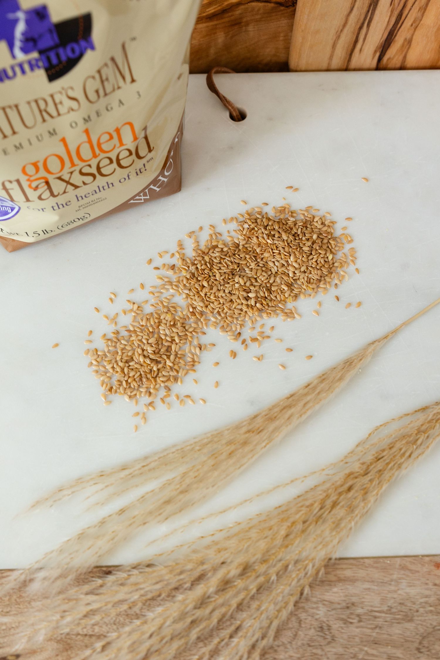 flax seeds on a white cutting board with decorative wheat and the bag flat lay