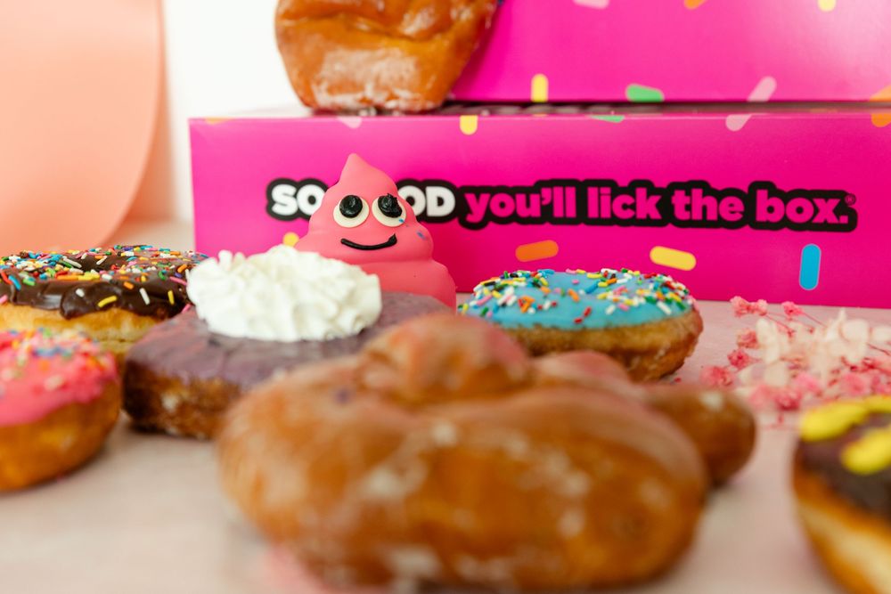 pink box donuts in foreground with pink boxes in the background. focus on a pink poop donut