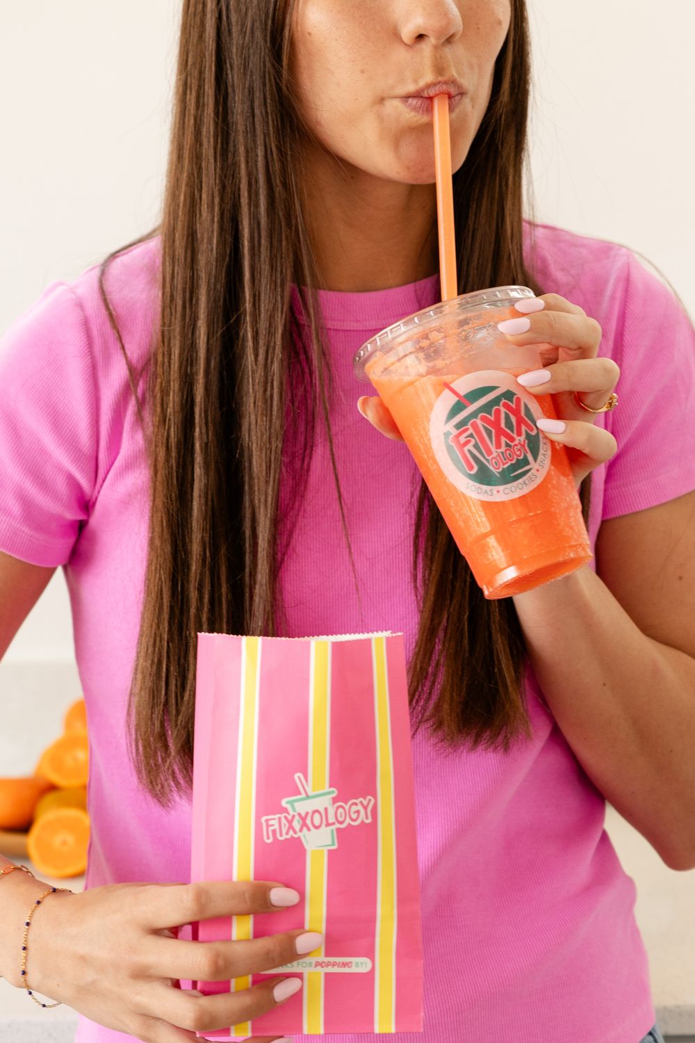 woman close up drinking a soda from a clear cup and straw holding a bag of popcorn