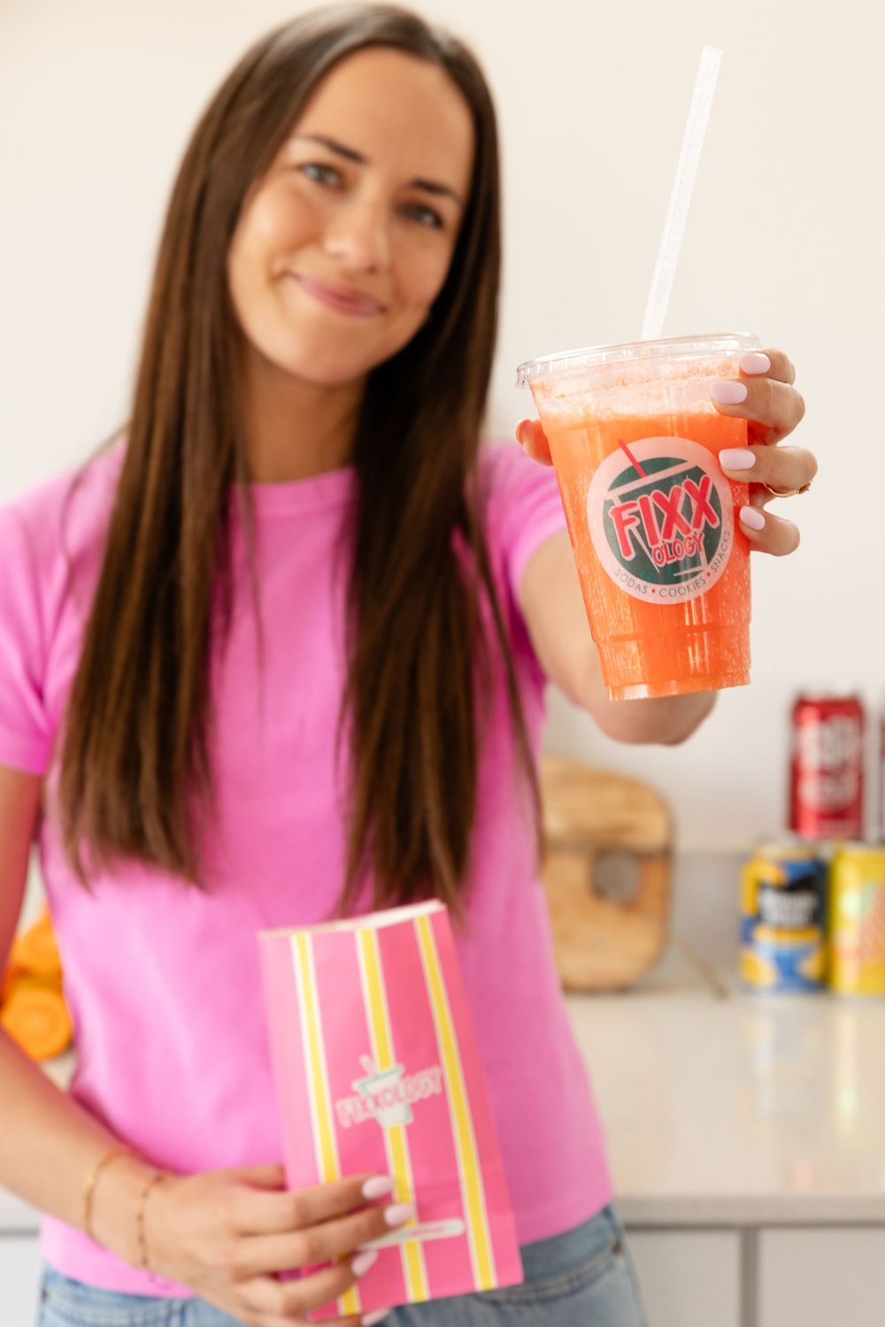 woman holding her drink in a clear cup and straw to the camera with a bag of popcorn smiling