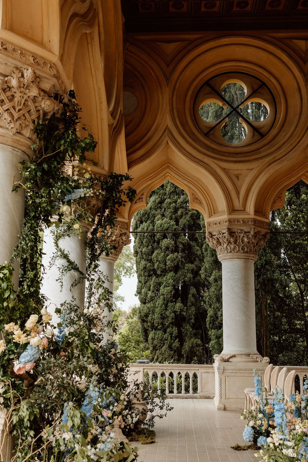 Elegant classical colonnade with ornate columns and arches decorated with lush greenery at a luxurious venue.