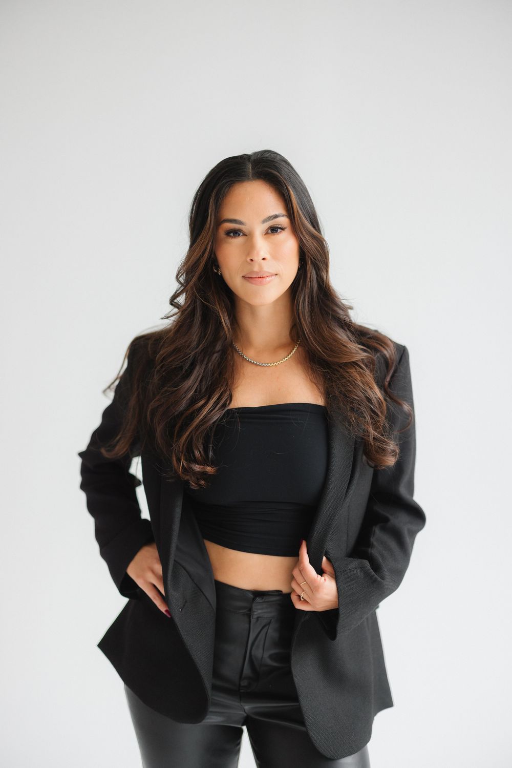 Fashionable model in black blazer and crop top poses against white background in professional studio photos.